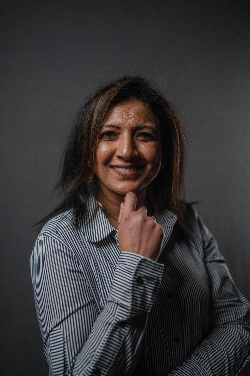 Rashmi Chanduraj in a studio portrait, smiling, hand to her chin
