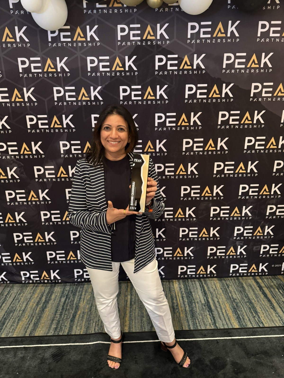 Rashmi holding an award in front of a PEAK Partnership backdrop