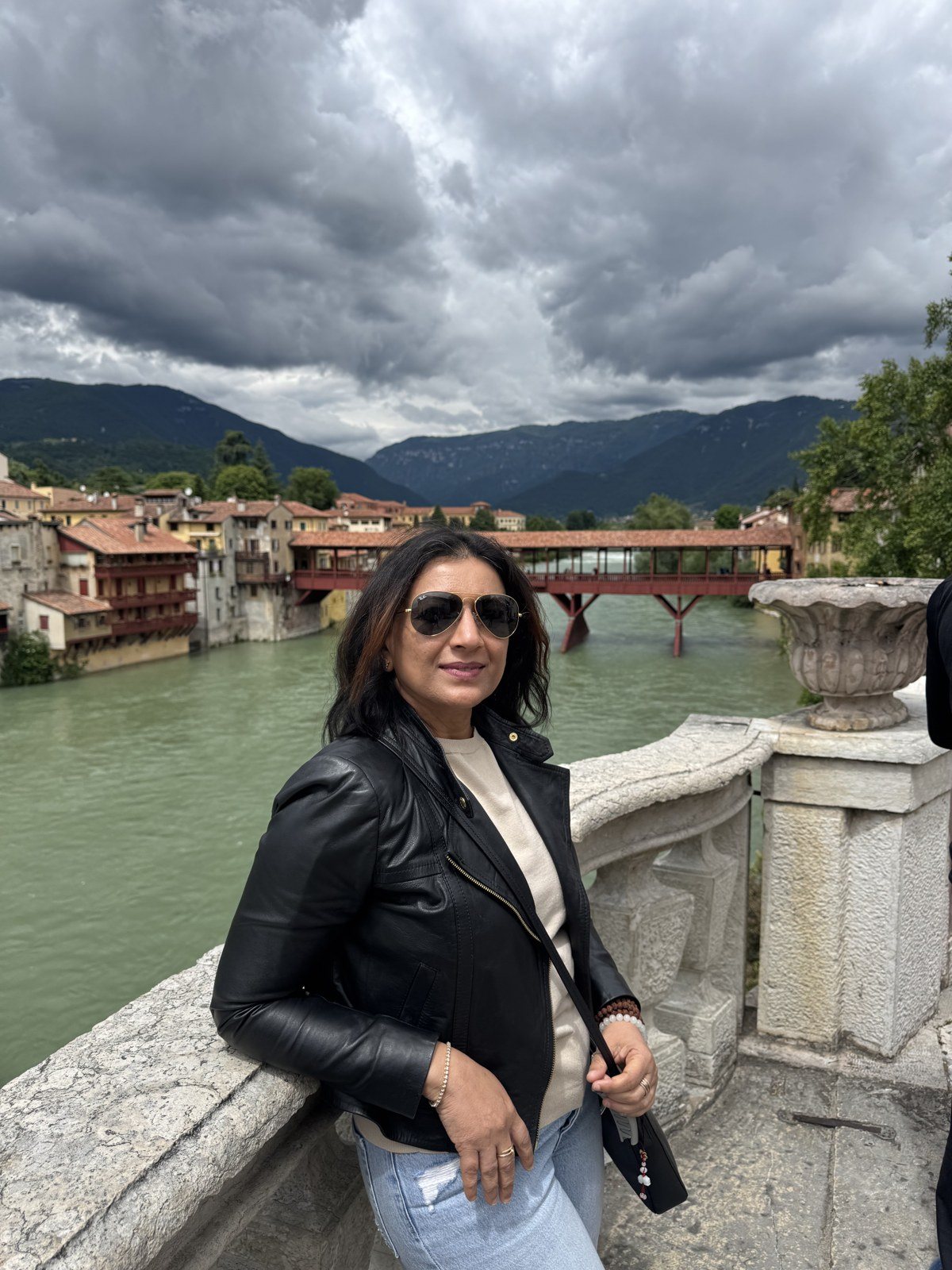 Rashmi leaning on a stone balustrade above a river town in Italy
