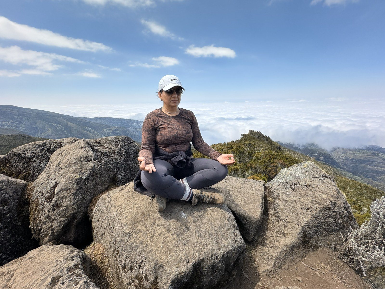 Rashmi seated cross-legged on a boulder above the clouds